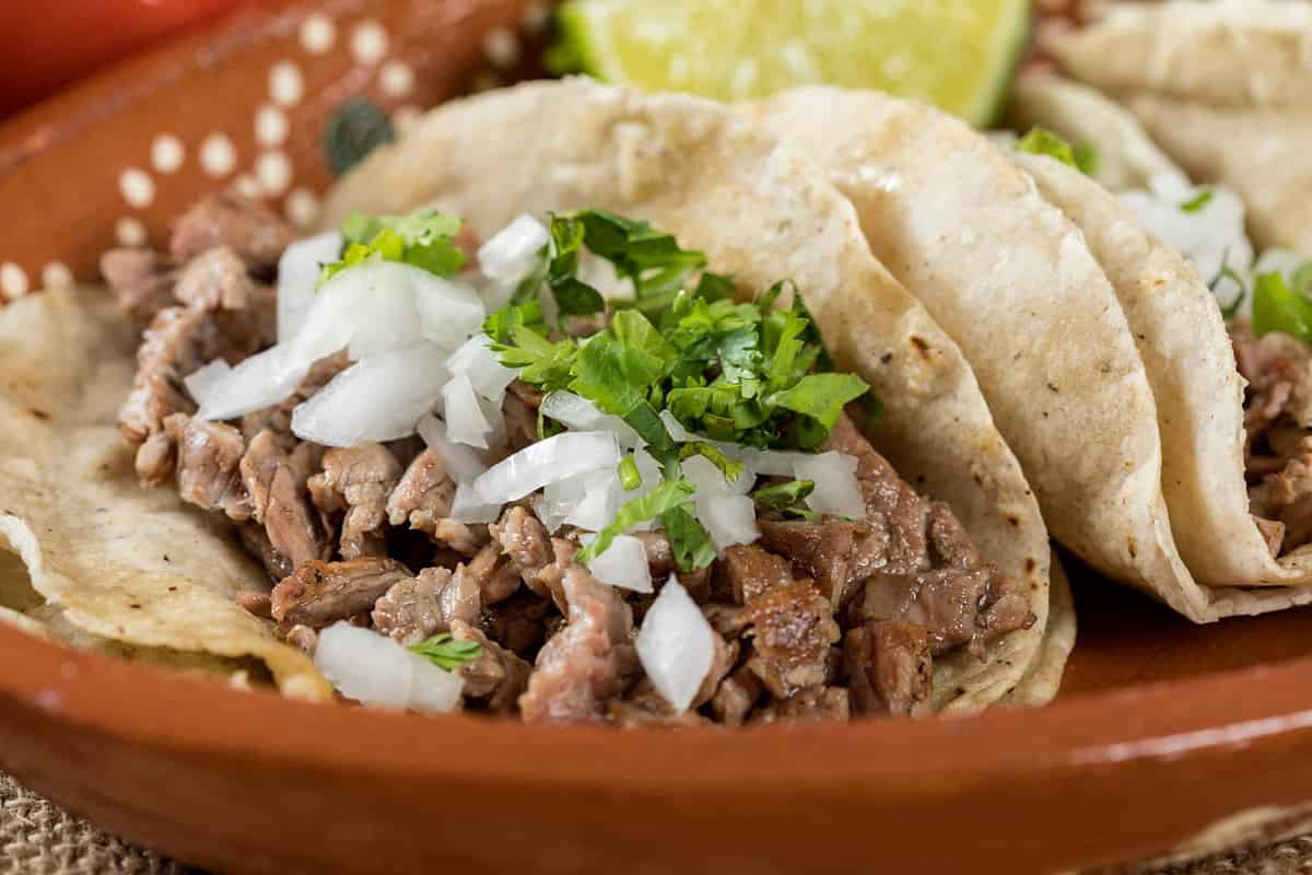 Typical Mexican food dishes with sauces on colorful table. Roast beef tacos