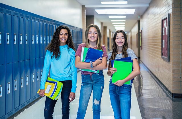 Group of Junior High school Students standing together in a school hallway. Female classmates smiling and having fun together during a break at school
