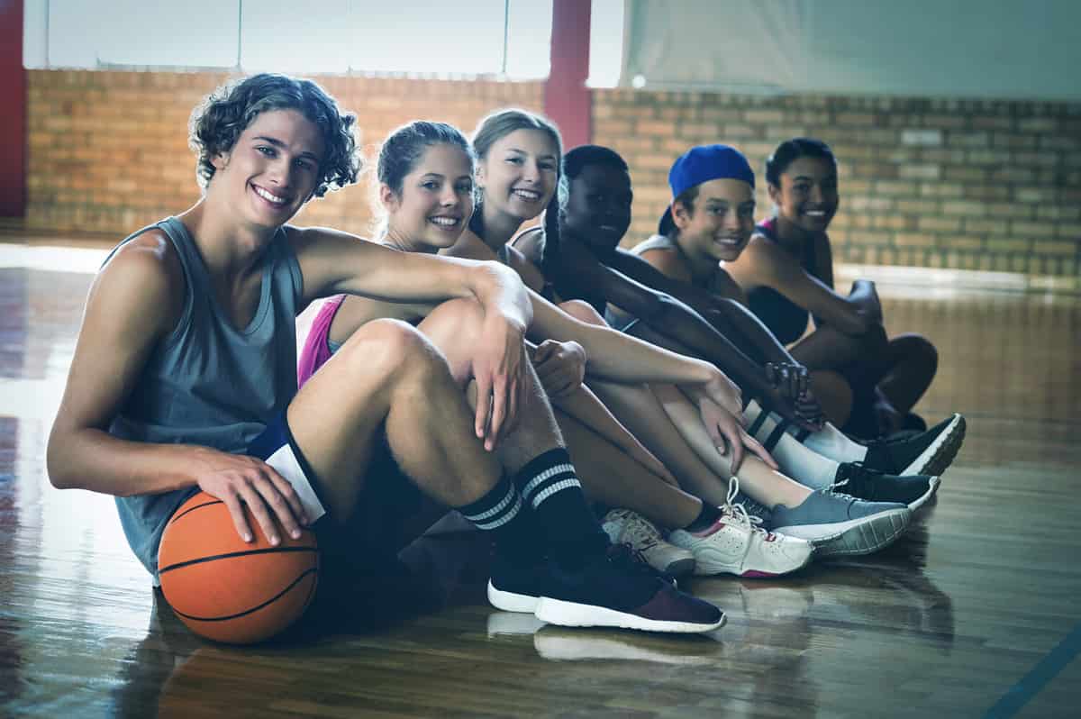 Portrait of high school kids sitting on the floor in basketball court indoors