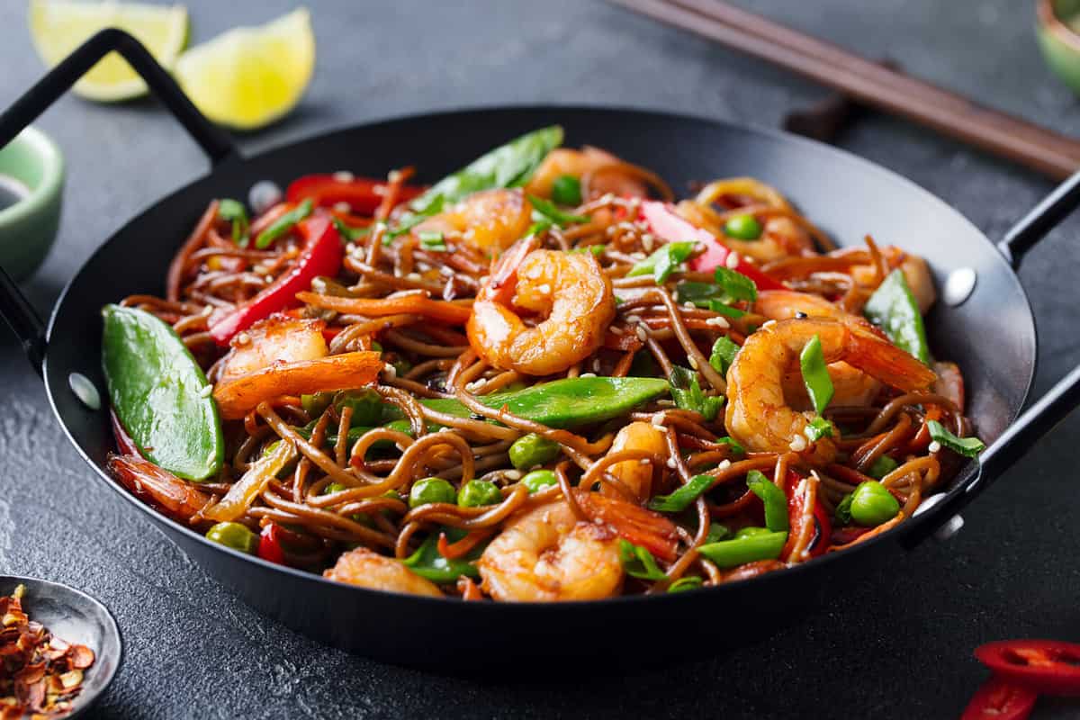 Stir fry noodles with vegetables and shrimps in black iron pan. Slate background. Close up.