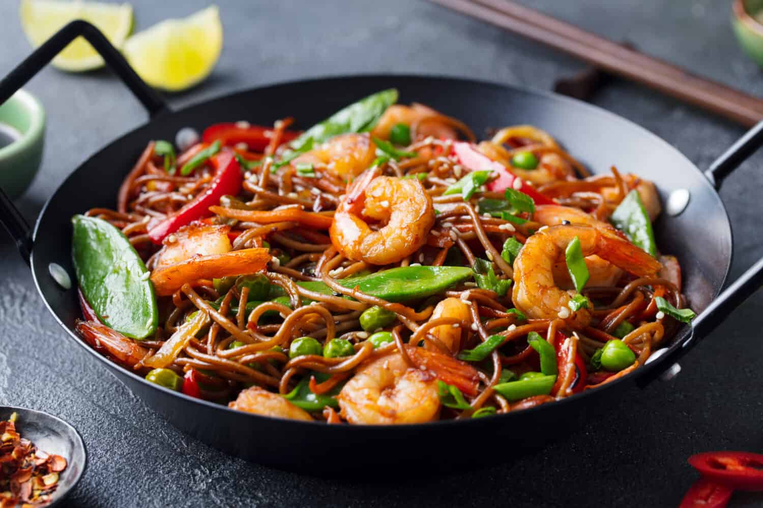 Stir fry noodles with vegetables and shrimps in black iron pan. Slate background. Close up.