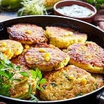 fried corn fritters in a skillet with yogurt dipping sauce and fresh sweet corn in cob on an old wooden kitchen table, close-up