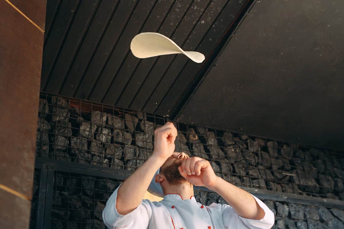 Skilled chef preparing dough for pizza rolling with hands and throwing up