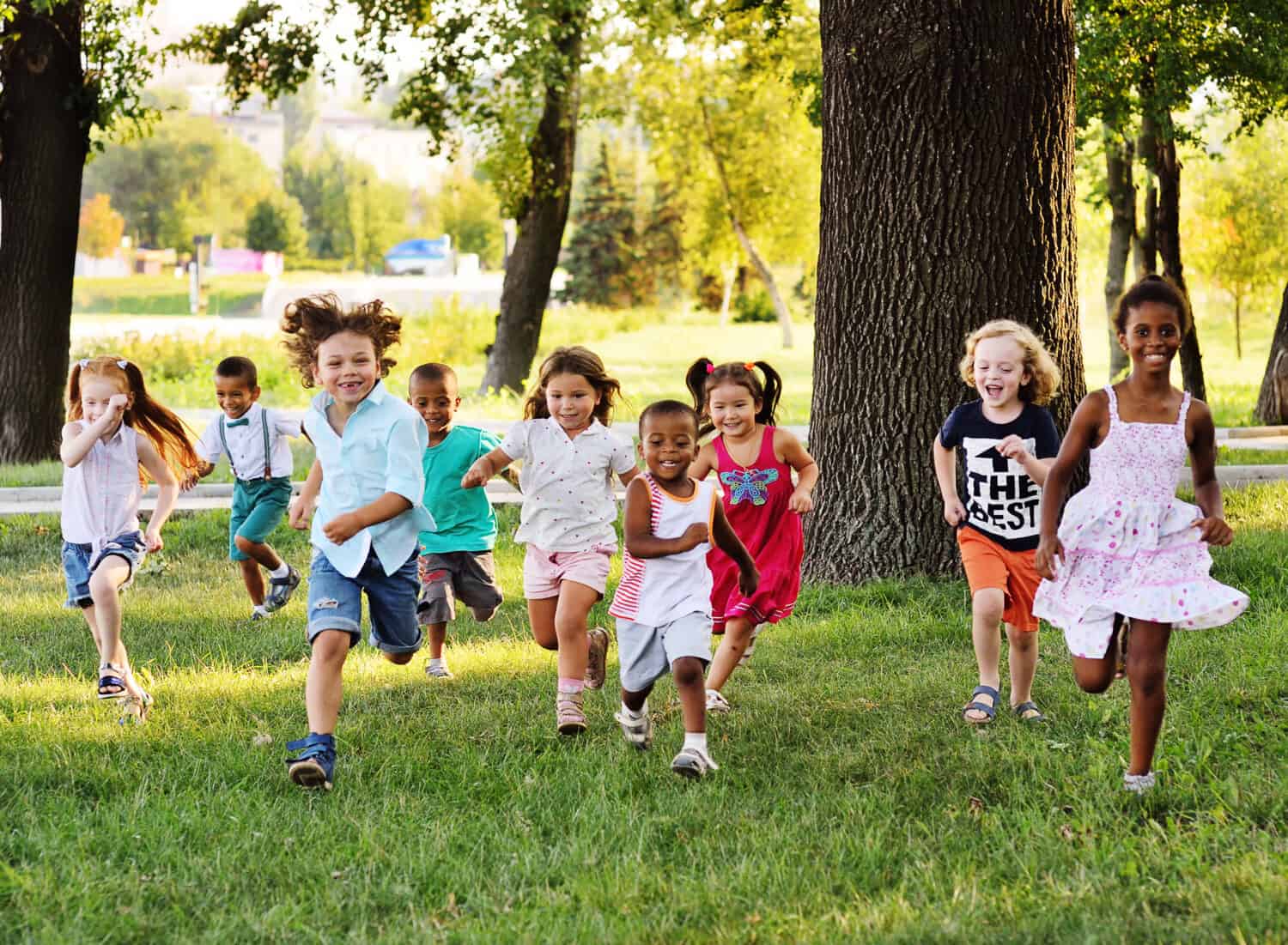 A group of happy children of boys and girls run in the Park on the grass on a Sunny summer day . The concept of ethnic friendship, peace, kindness, childhood.