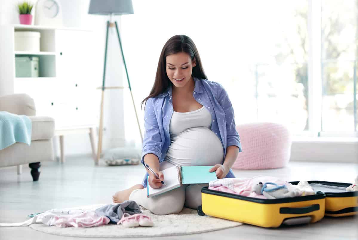 Pregnant woman writing packing list for maternity hospital at home