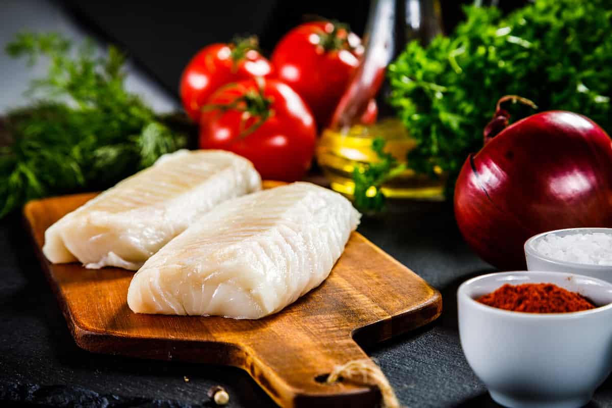 Fresh raw cod with herbs served on black stone on wooden table