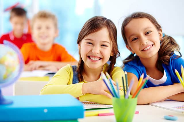 Portrait of two diligent girls looking at camera at workplace with schoolboys on background