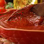 Freshly prepared pasta or pizza sauce in bowl with wooden spoon. Tomatoes, olive oil, and herbs in background. Closeup with shallow dof. Selective focus on sauce in spoon.