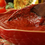 Freshly prepared pasta or pizza sauce in bowl with wooden spoon. Tomatoes, olive oil, and herbs in background. Closeup with shallow dof. Selective focus on sauce in spoon.