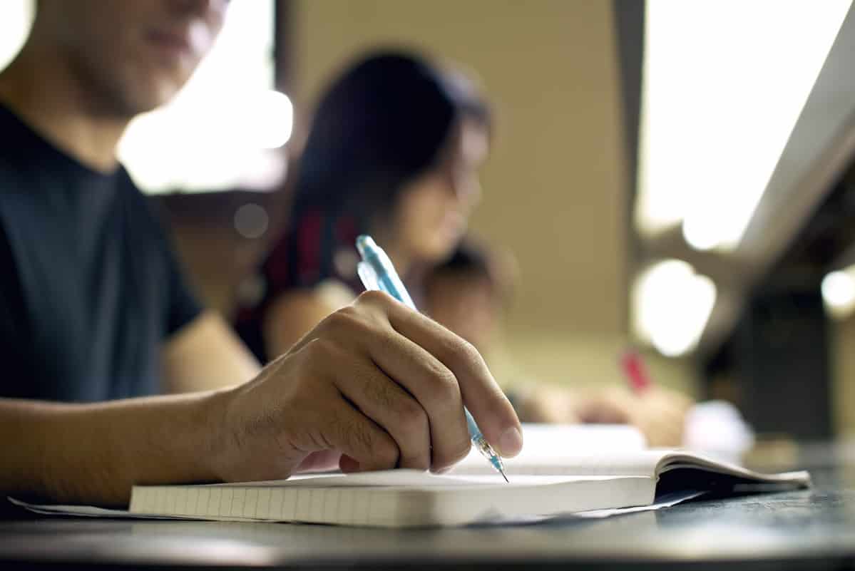 Students doing homework and preparing exam at university, closeup of young man writing in college library