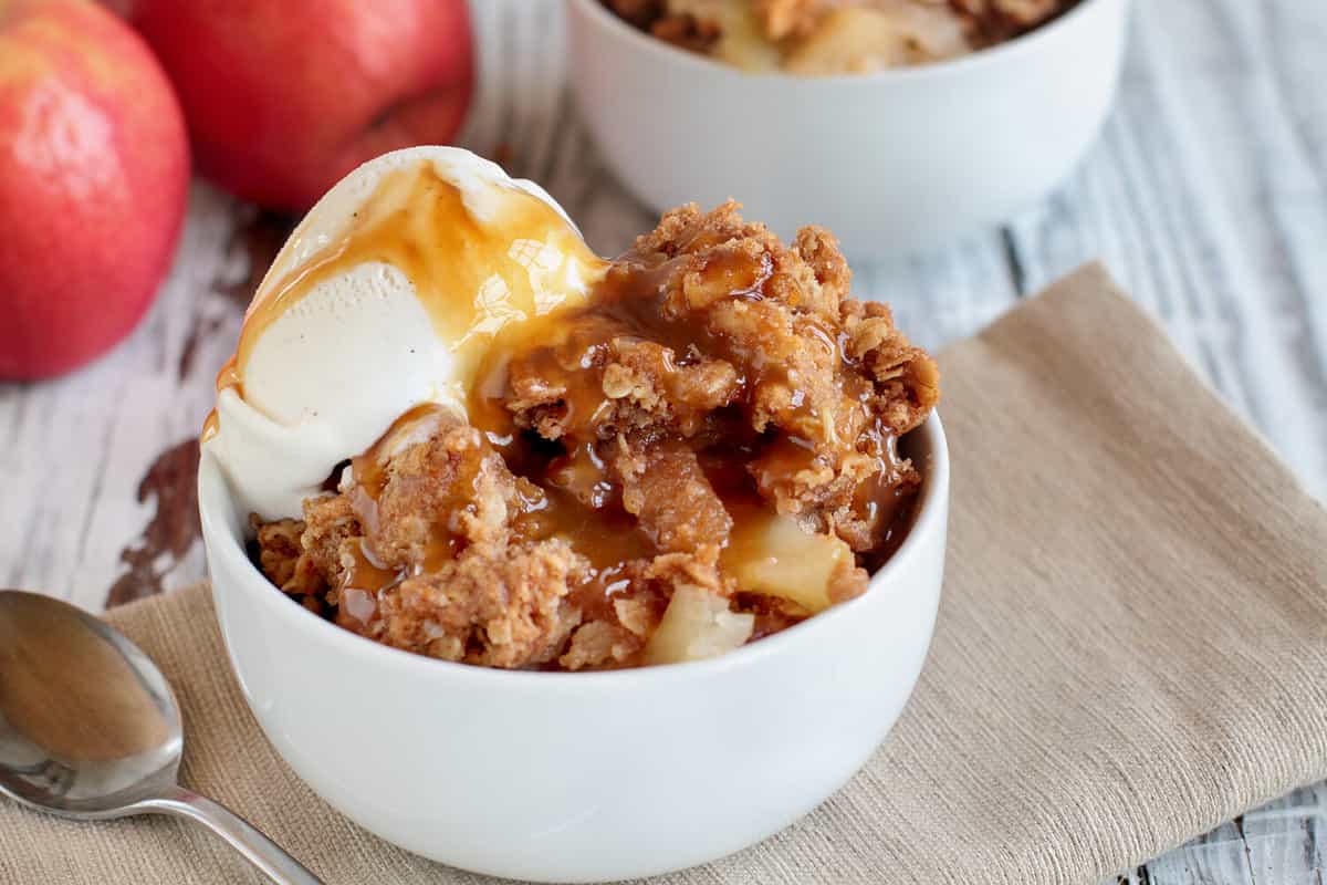 Fresh hot homemade apple crisp or crumble with crunchy streusel topping topped with vanilla bean ice cream and Caramel Sauce. Selective focus with blurred background.