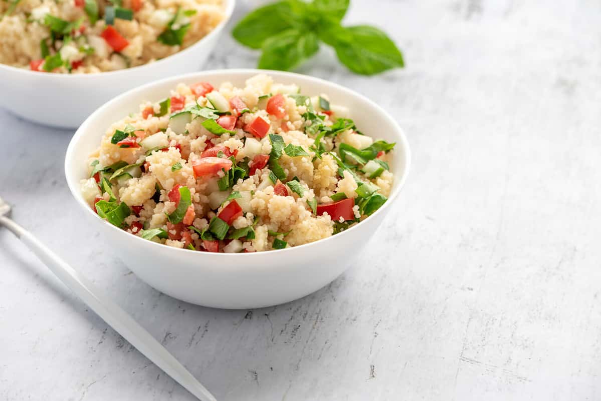 Tabbouleh - Arabian vegetarian salad made of couscous, tomatoes, cucumbers, parsley, onions and lemon juice. Couscous with vegetables in a white bowl on the table.
