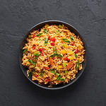 Veg Schezwan Fried Rice in black bowl at dark slate background. Vegetarian Szechuan Rice is indo-chinese cuisine dish with bell peppers, green beans, carrot. Top view