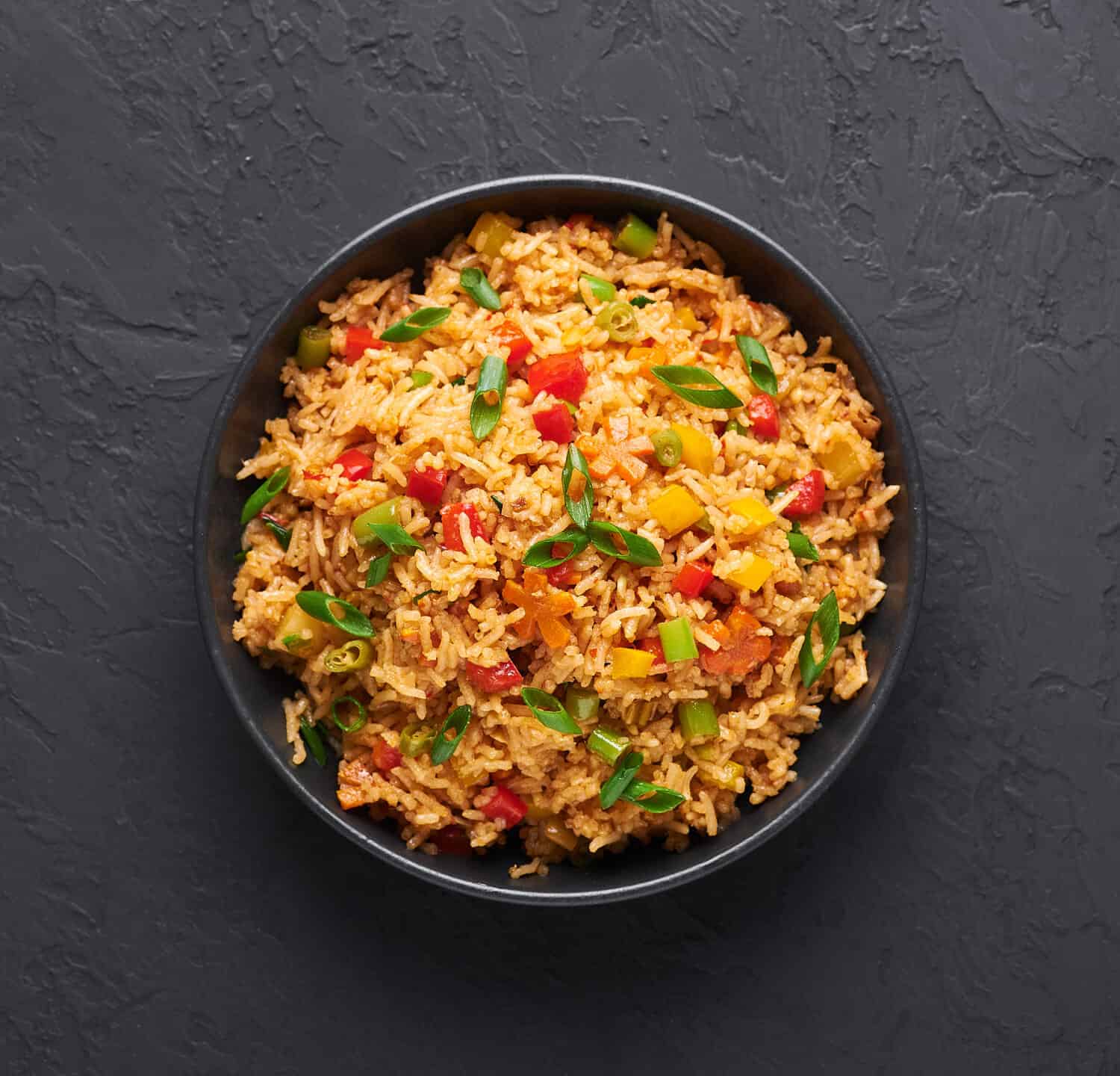 Veg Schezwan Fried Rice in black bowl at dark slate background. Vegetarian Szechuan Rice is indo-chinese cuisine dish with bell peppers, green beans, carrot. Top view