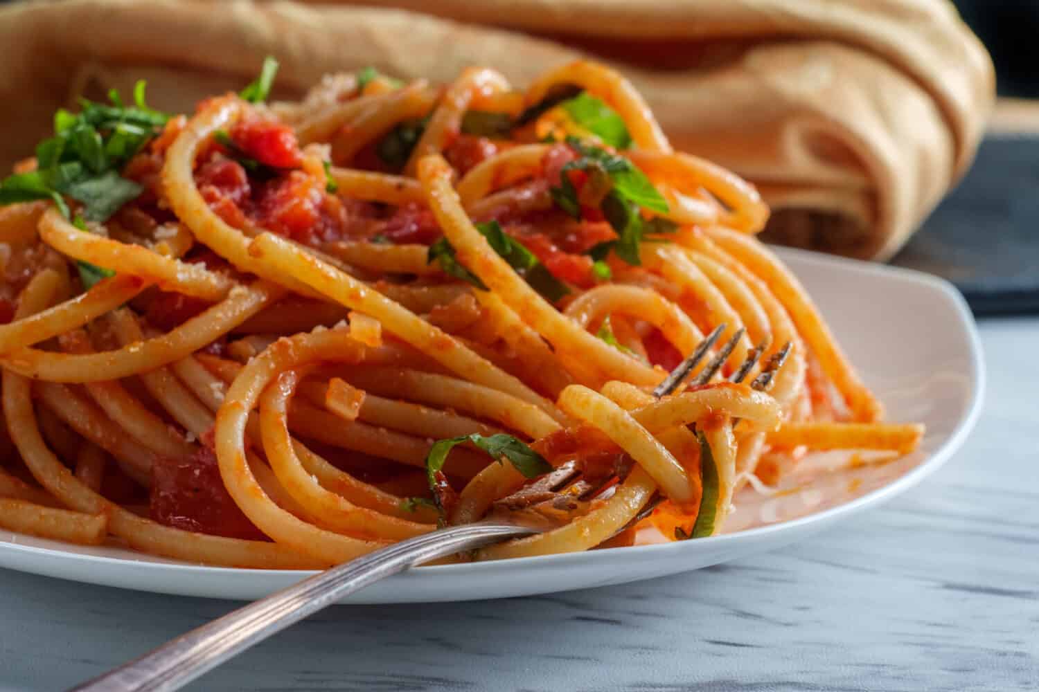 Authentic Italian bucatini all'amatriciana made with san marzano tomatoes and garnished with fresh chopped basil and grated pecorino romano cheese