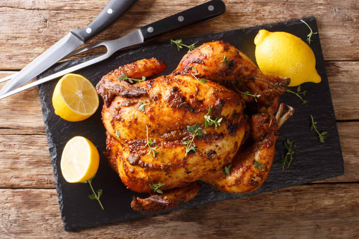 Homemade chicken rotisserie with thyme, lemon closeup on a slate board on the table. Horizontal top view from above