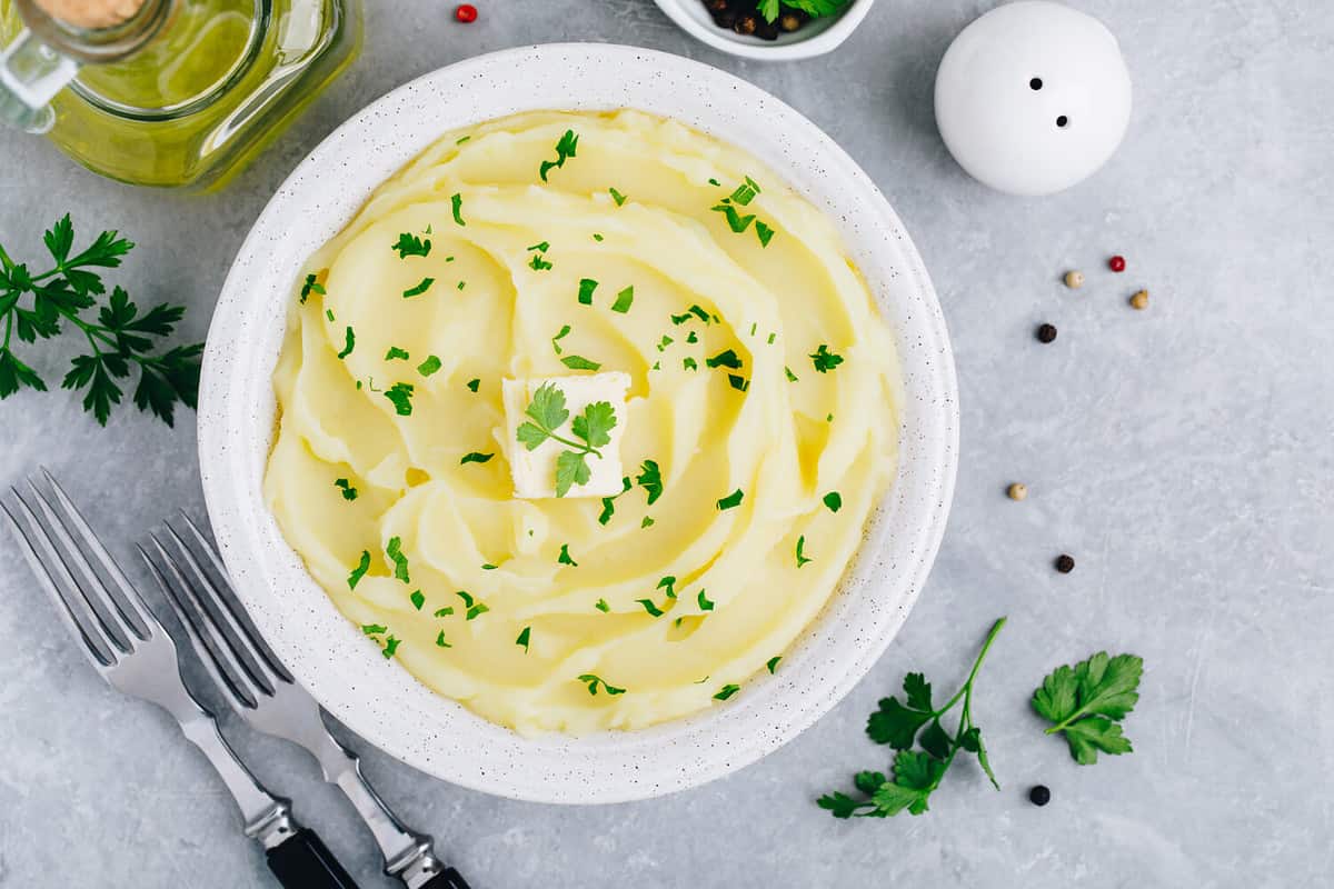 Mashed Potatoes with butter and fresh parsley in a white bowl on gray stone concrete background. Top view, copy space