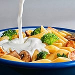 Pouring white cream sauce over plate of pasta.