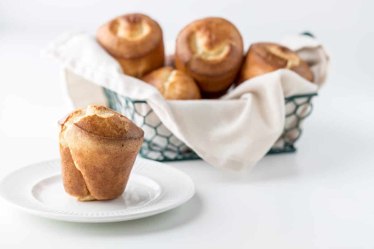 Close up of a basket filled with popovers with a popover on a plate in front.