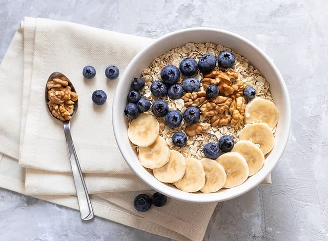 Oatmeal. Porridge with bananas, blueberries and walnut for healthy breakfast or lunch. Natural ingredients. Flat lay design on linen napkin and cement background