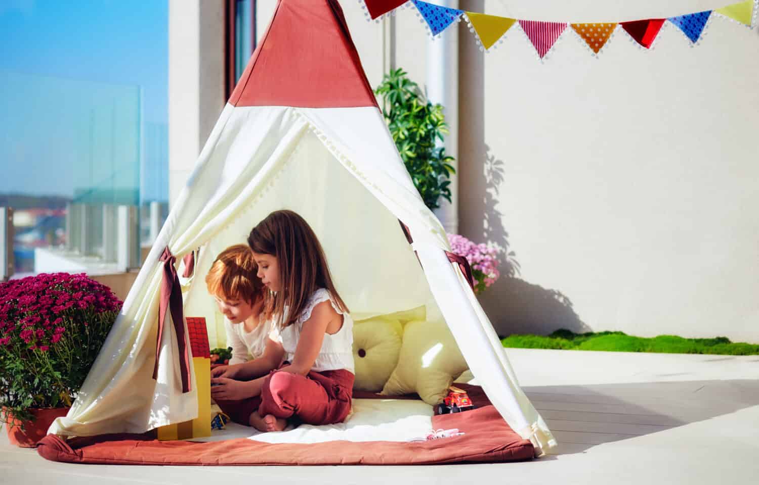 cheerful kids are playing in teepee tent on a sunny patio