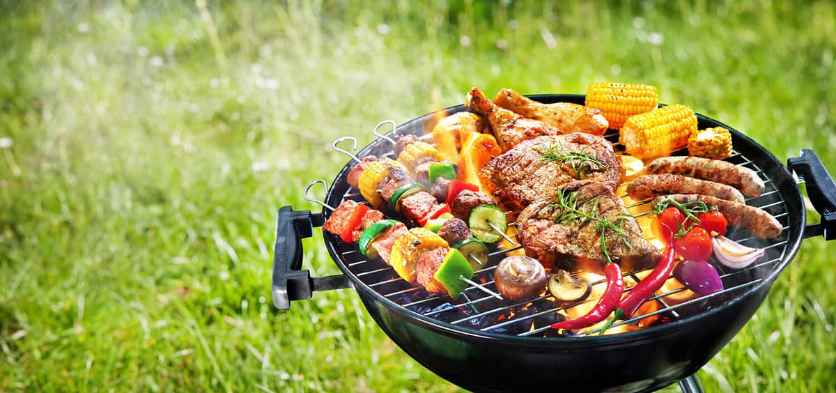 Assorted delicious grilled meat with vegetables on barbecue grill with smoke and flames in green grass