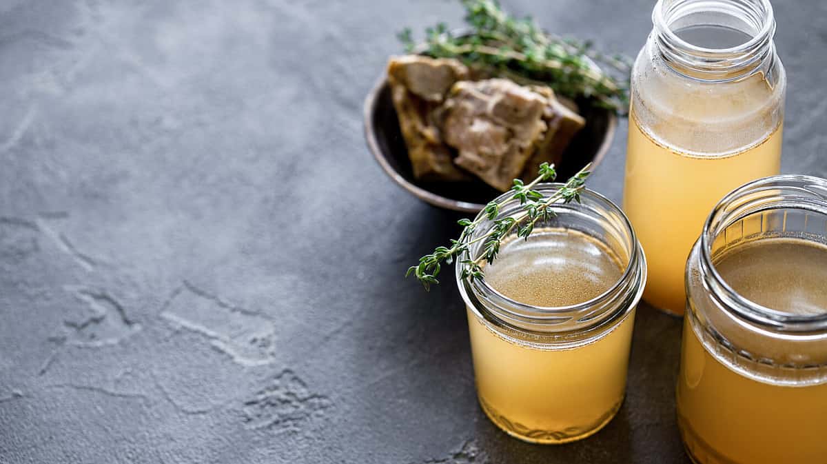 Glass jar with yellow fresh bone broth on dark gray background. Healthy low-calories food is rich in vitamins, collagen and anti-inflammatory amino acids