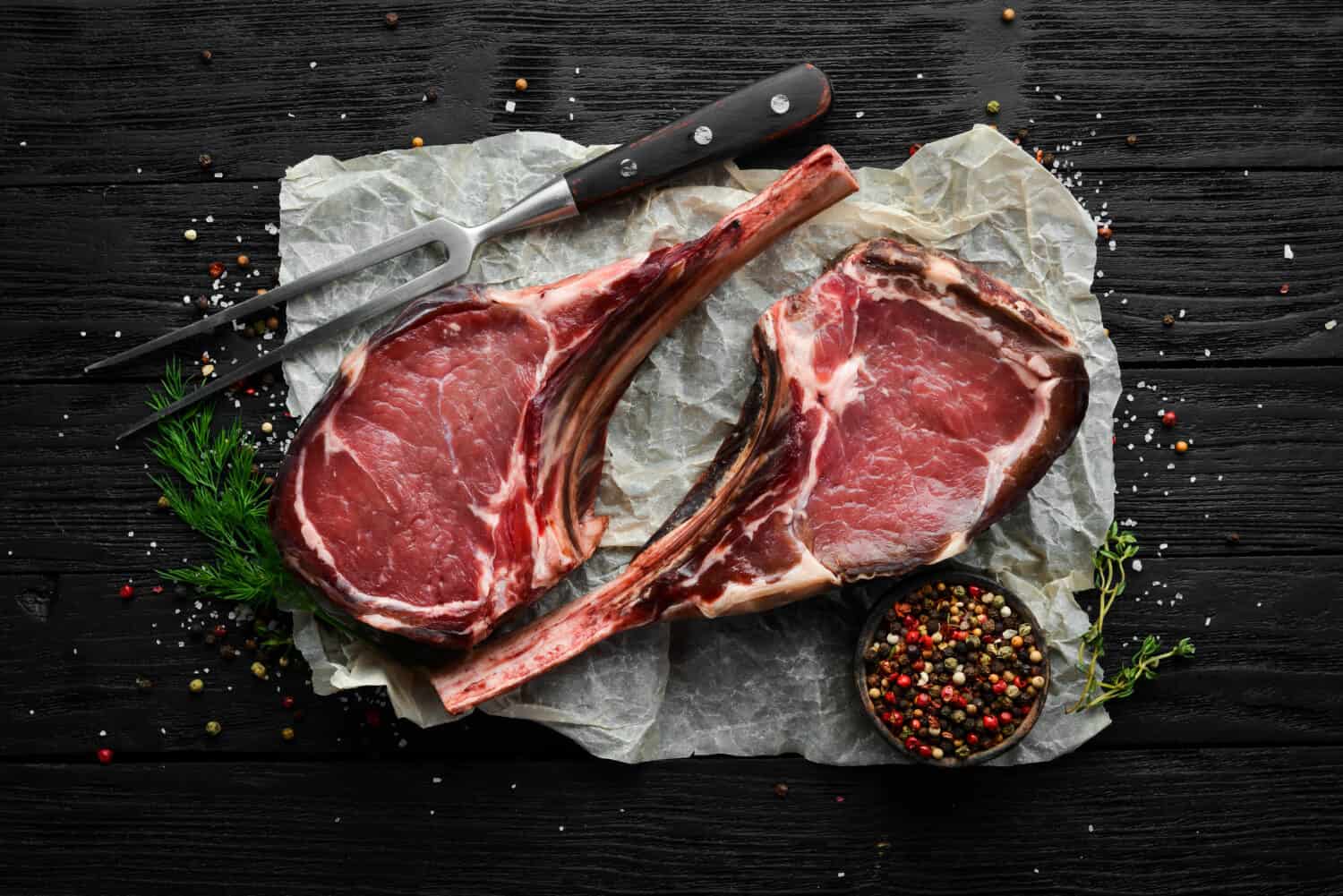 Dry aged raw tomahawk beef steak with spices. On a black wooden background. Top view. Free copy space.