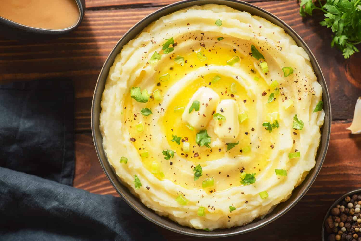 Delicious creamy mashed potatoes with butter, fresh herbs and freshly-cracked black pepper. Top view with close up.