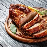 Sunday roasted pork tenderloin, juicy and succulent oven-baked piece of meat rubbed with mustard and spices: rosemary, bay leaf, lime juice, and pepper on a wooden background, close-up, top view