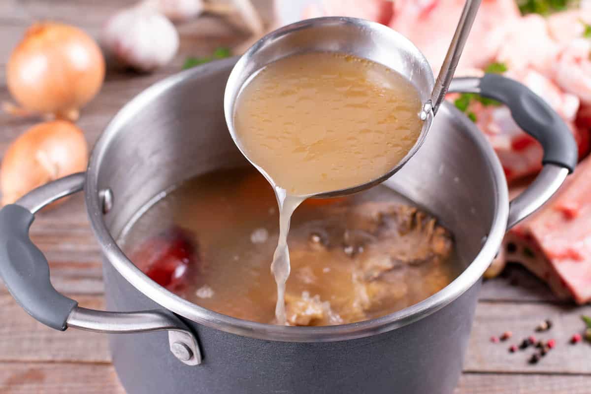 Saucepan with bouillon with a ladle on the table. Bone broth