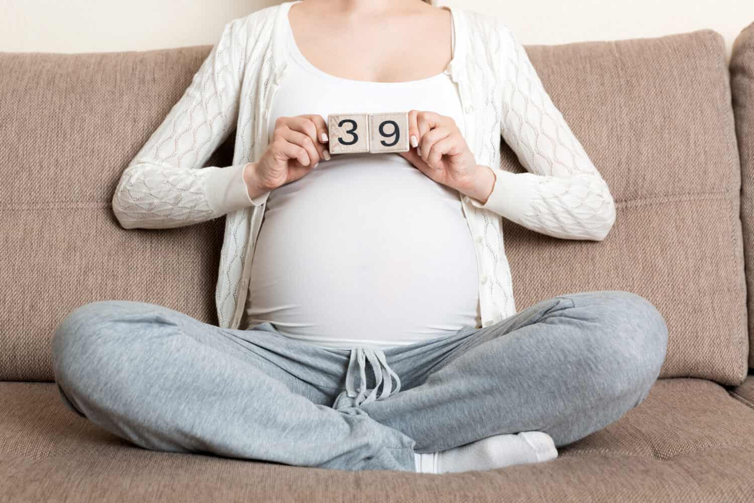 Pregnant woman in white underwear on bed in home holding calendar with weeks 39 of pregnant. Maternity concept. Expecting an upcoming baby.