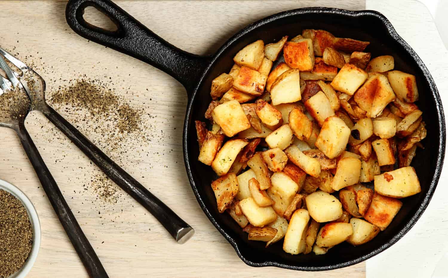 Ranch Potatoes in Cast Iron Skillet on Cutting Board with Black Pepper.