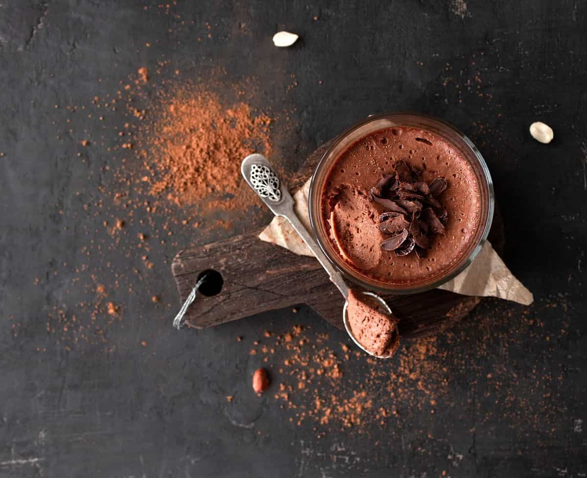 Vegan chocolate mousse glass on a wooden board with a spoon on a dark background. Top view. Flat lay