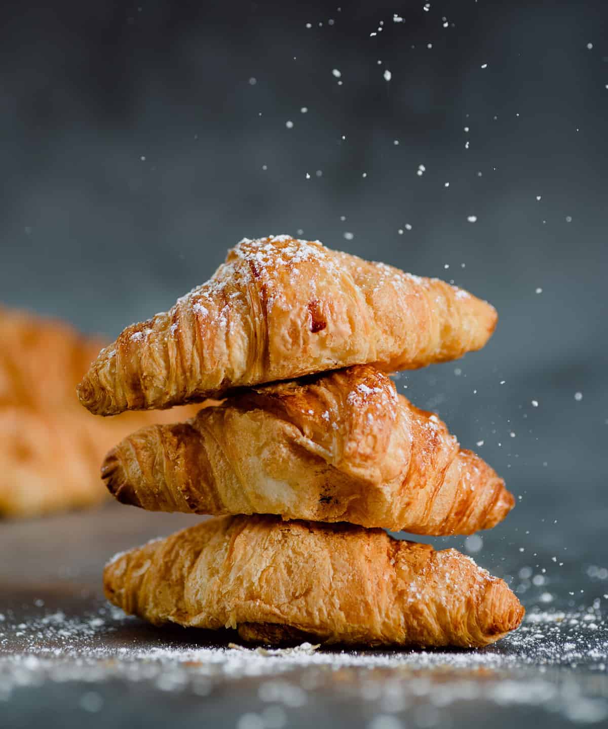 Close up of pile of delicious croissants on a dark background. Homemade croissants. Sugar glass falling. Vertical.