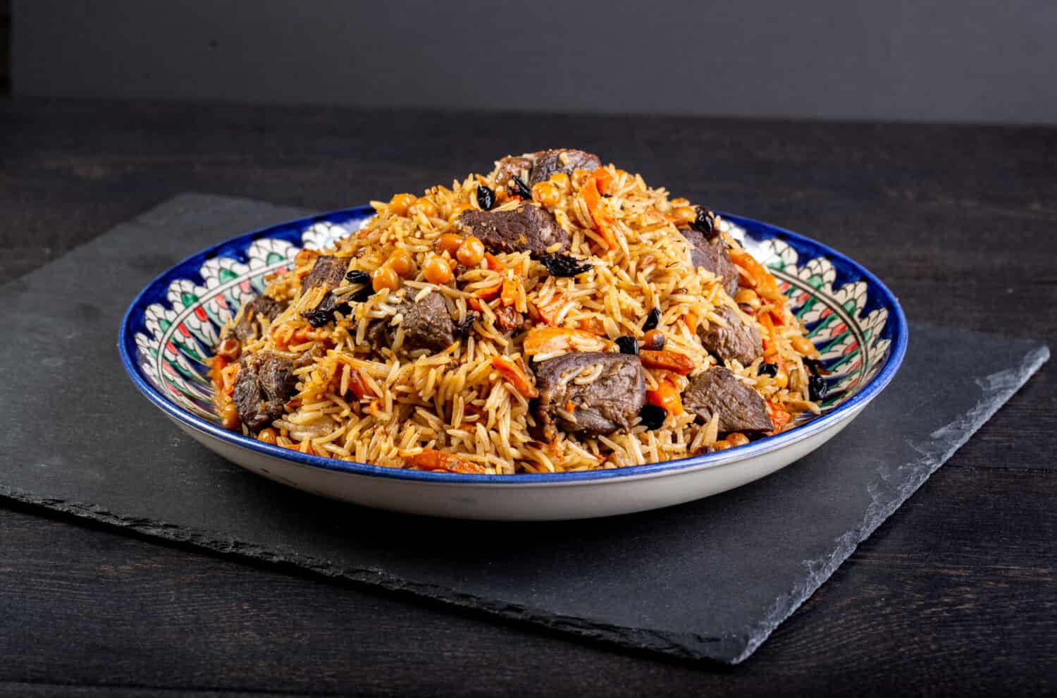 The concept of oriental cuisine. Assorted Uzbek food set, pilaf, samsa, lagman, manta, shurpa central asia food. Homemade Uzbek pilaf or plov from lamb served in cast iron cookware