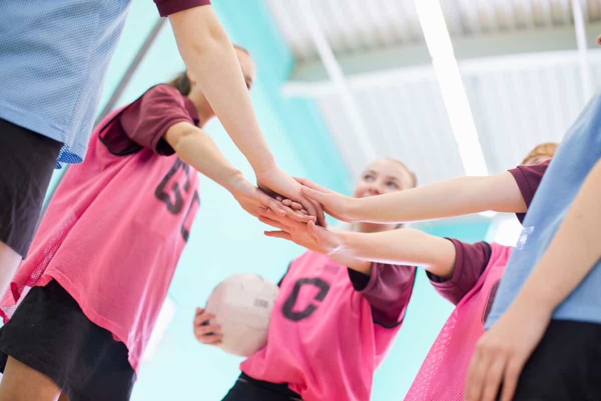 Low angle shot of high school students touching hands in a huddle before a volleyball game.