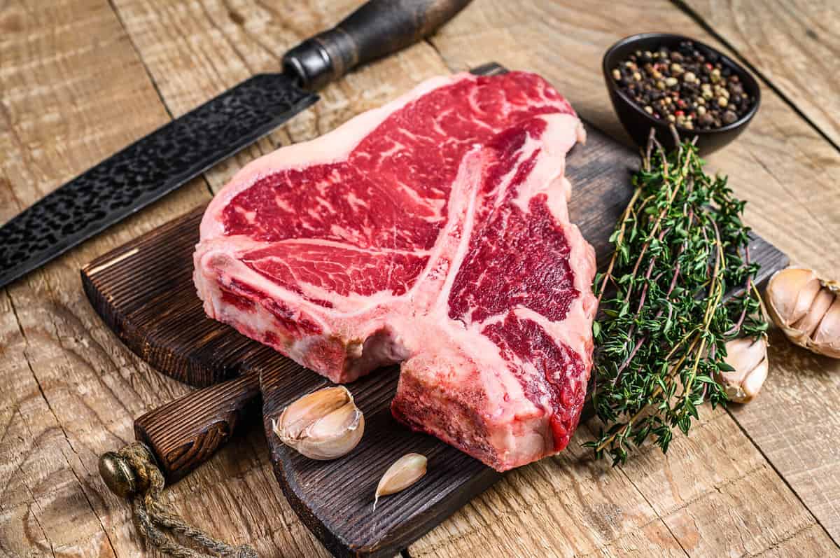 Raw Porterhouse or T-bone beef meat Steak with herbs on a wooden cutting board. wooden background. Top view