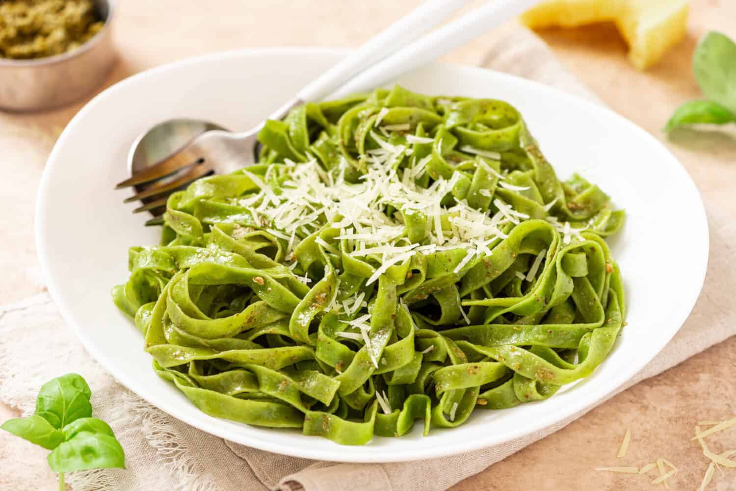 Spinach pasta with pesto sauce and grated cheese in a white plate on a light background. Italian food, Mediterranean cuisine. Green tagliatelle pasta with pesto and parmesan.