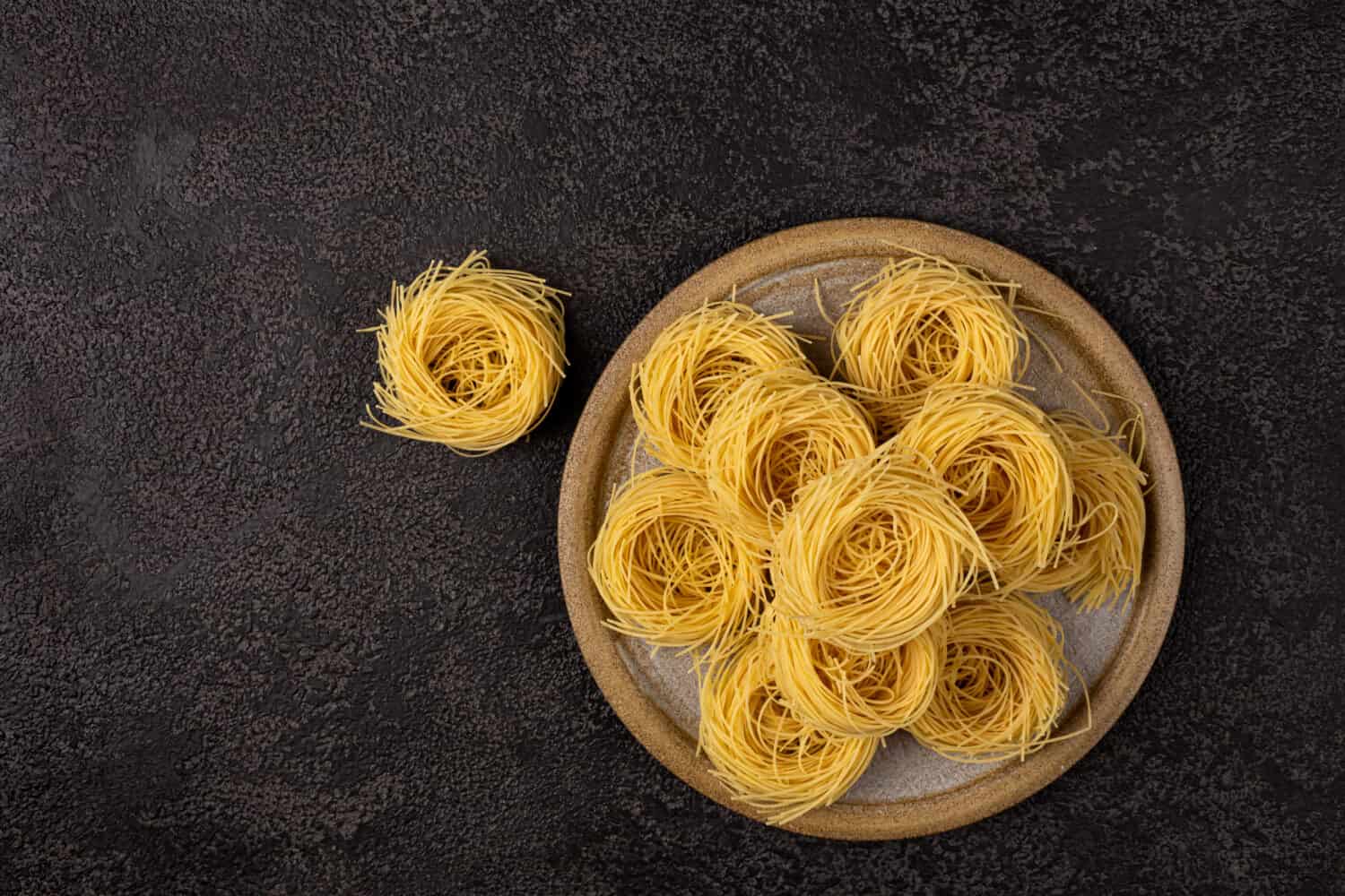 Capellini spaghetti on a ceramic plate on a dark structural background with space to copy. Spaghetti top view