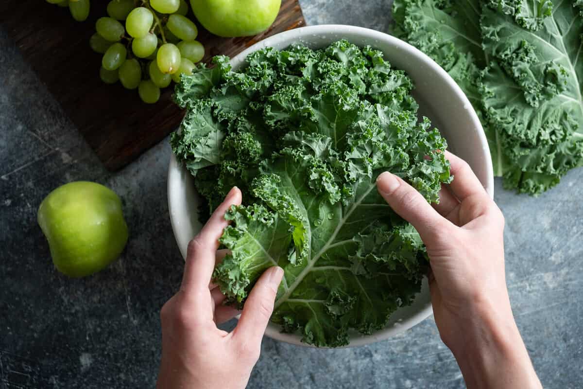 Female hands washing kale cabbage in bowl of water. Cooking healthy organic home grown vegan food, top view