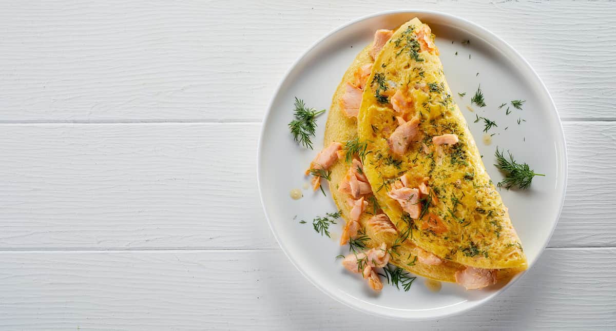 Top view of yummy omelet with salmon on plate served on white wooden table