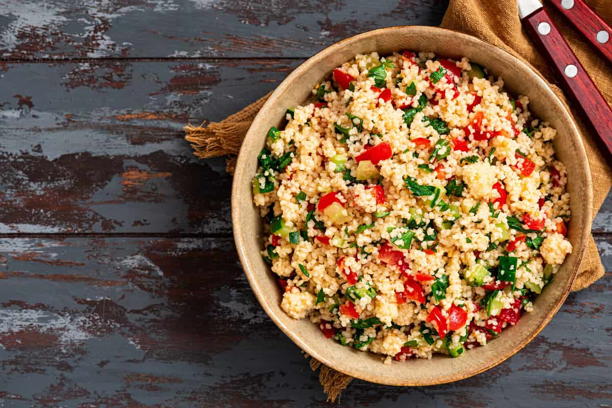 Vegan salad made of couscous, tomatoes, cucumbers, parsley and lemon juice. Couscous with vegetables in a bowl on a dark wooden background. Tabbouleh salad.