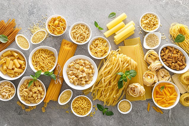 Gluten-Free Pasta. Various kinds of uncooked pasta and noodles over stone background, top view with copy space for text. Italian food culinary concept. Collection of different raw pasta on cooking table