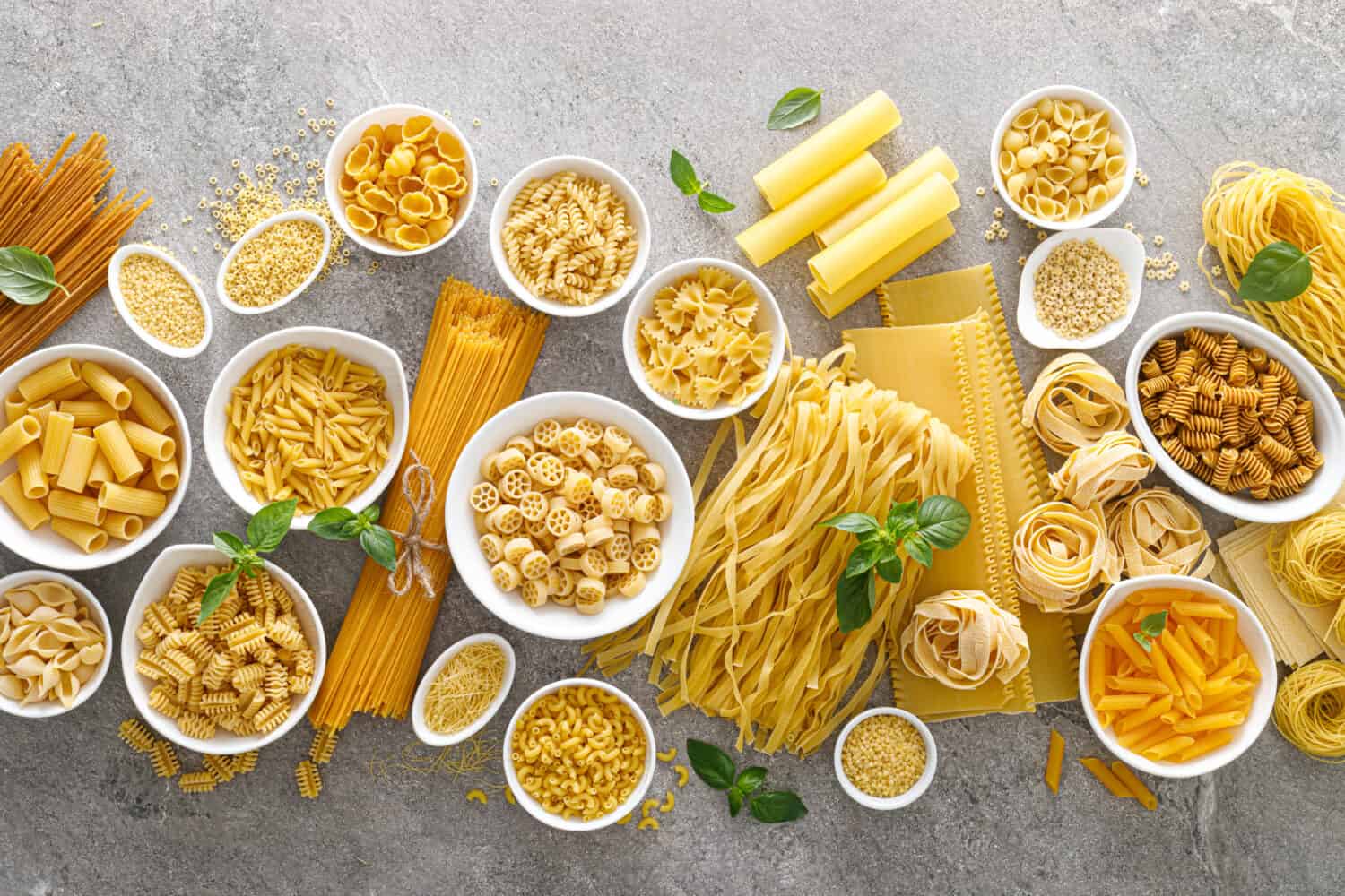 Gluten-Free Pasta. Various kinds of uncooked pasta and noodles over stone background, top view with copy space for text. Italian food culinary concept. Collection of different raw pasta on cooking table