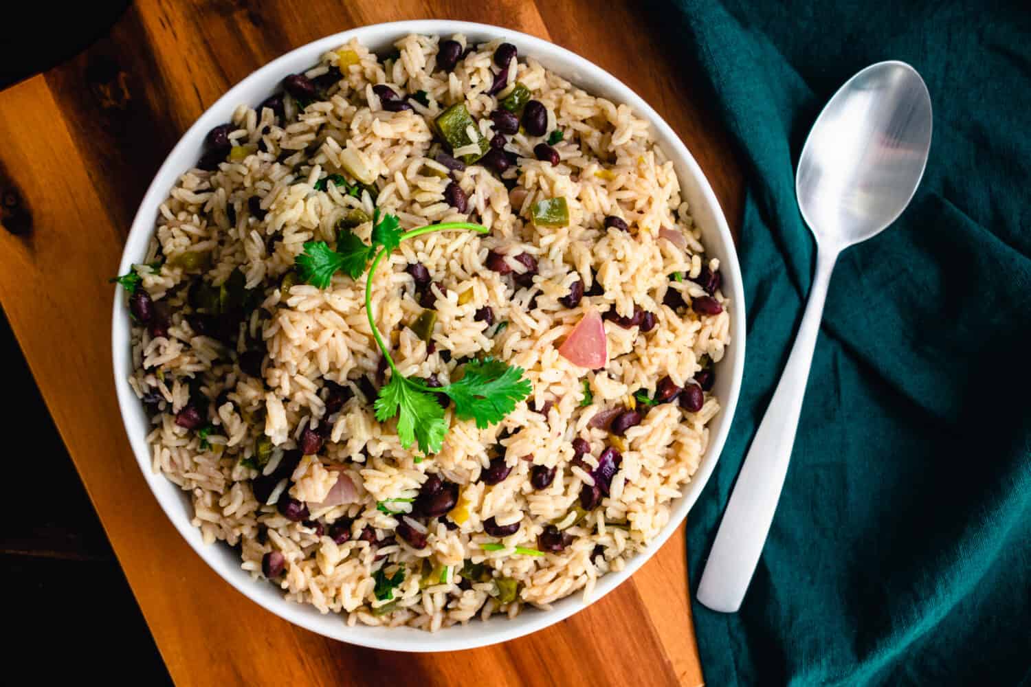 Cilantro Lime Rice with Black Beans in a Serving Bowl: A bowl of beans and rice garnished with cilantro and shown with a serving spoon and cloth napkin