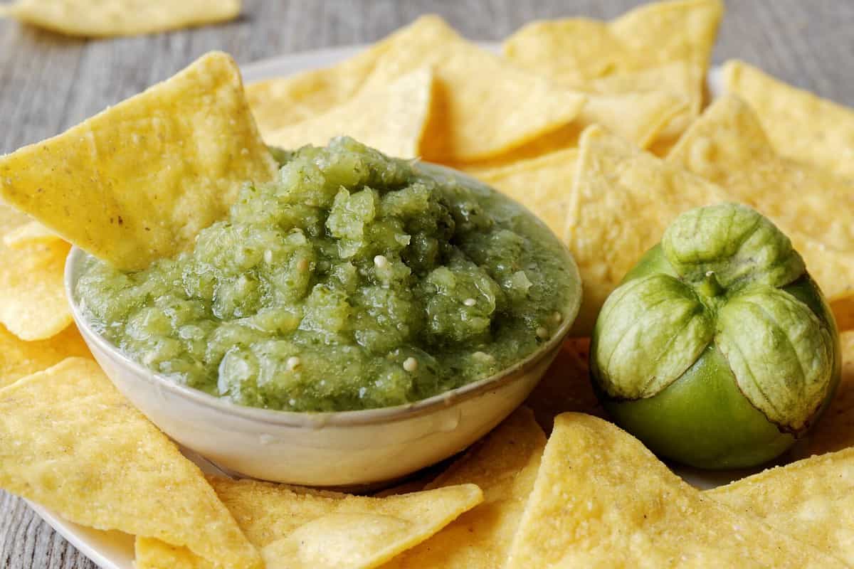 Green tomatillo salsa (salsa verde cruda) with corn tortilla chips nachos.