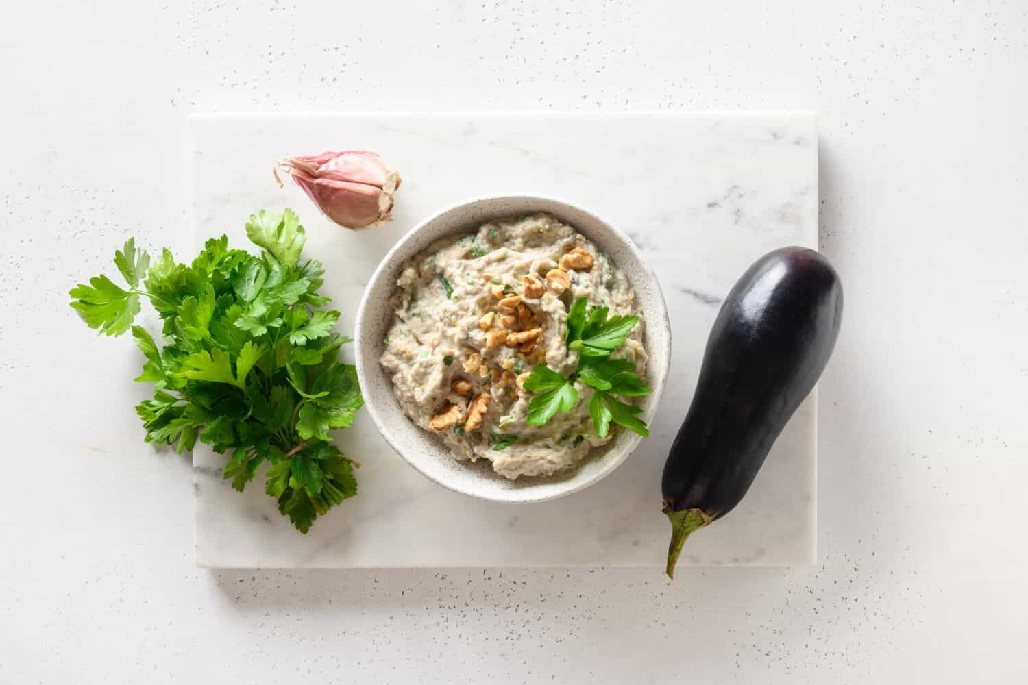 Baba ganoush appetizer of baked eggplant with parsley, garlic and olive oil on white background. Arabic cuisine. View from above.