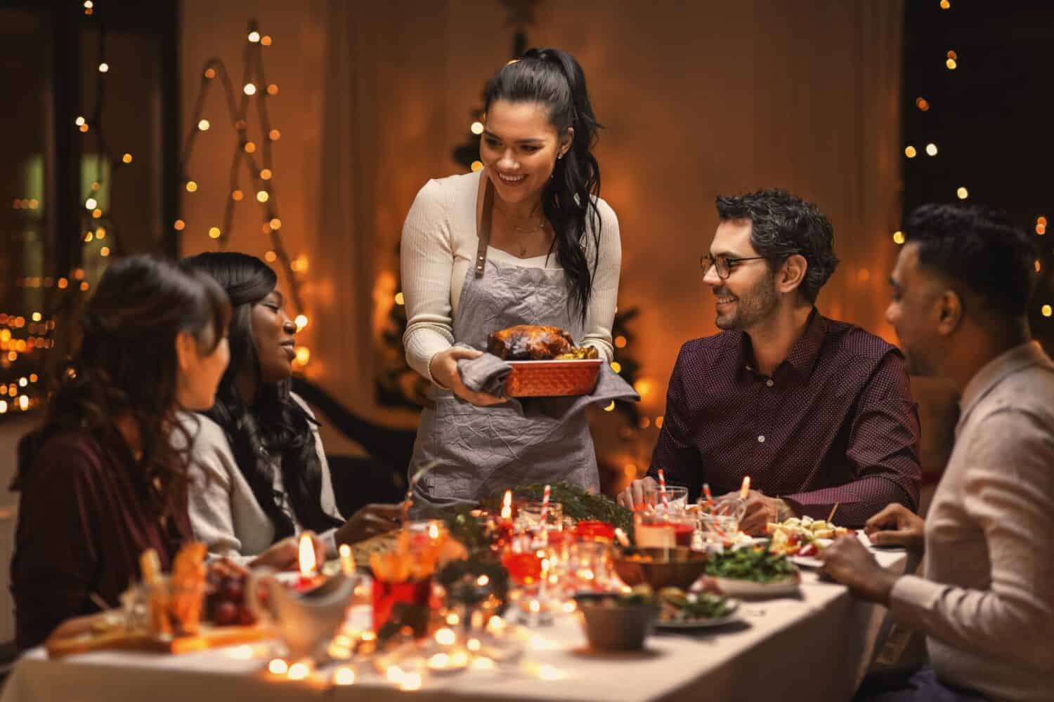 holidays and celebration concept - multiethnic group of happy friends having christmas dinner at home