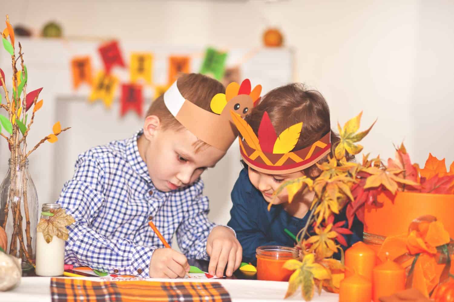 Girl and boy in paper turkey and native American hats writing I am thankful for. Celebrating Thanksgiving day. Diy craft art project.